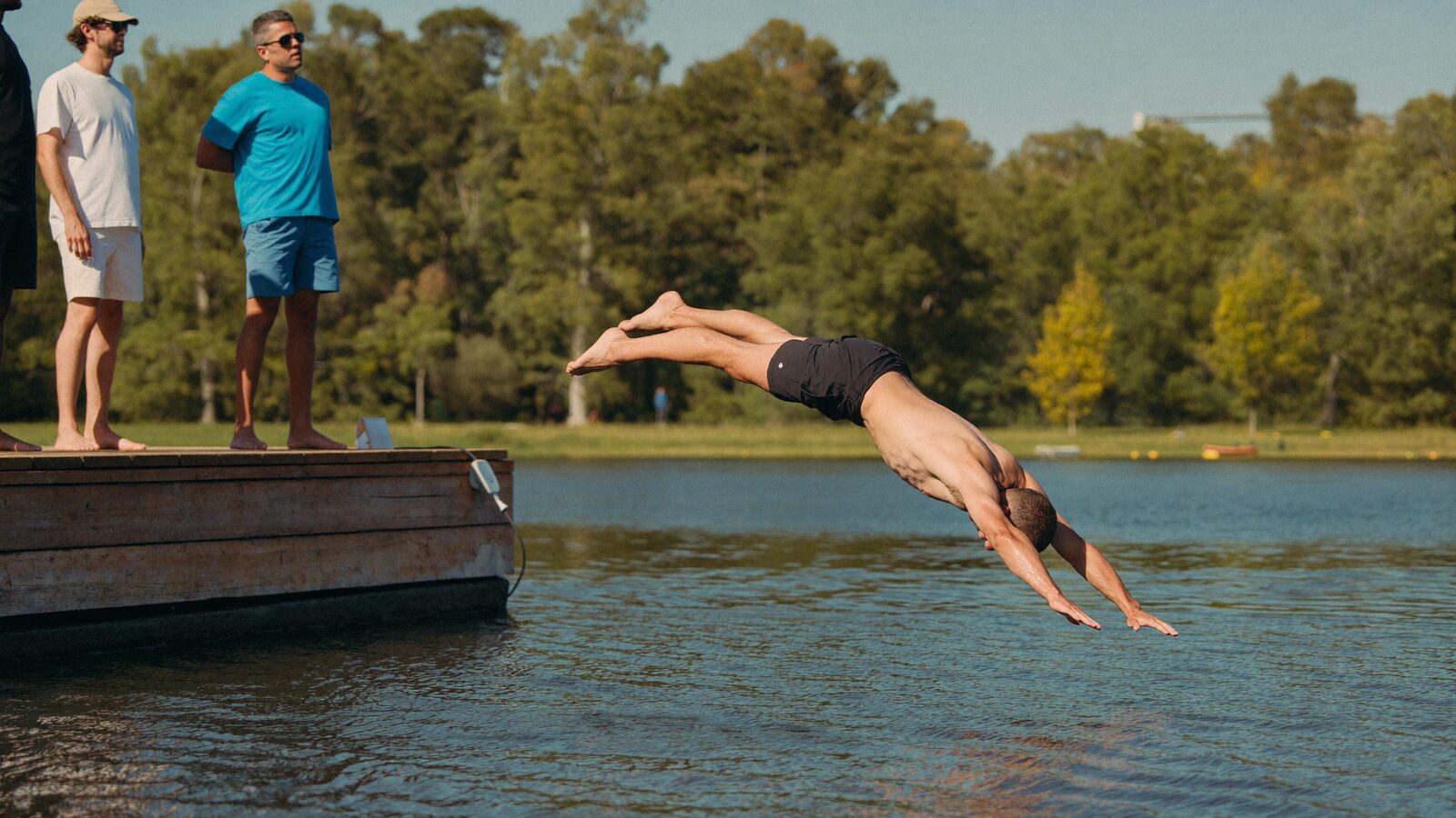 Man in his early 40s with thick, natural hair laughing as he walks out of a lake after a swim on a sunny summer day