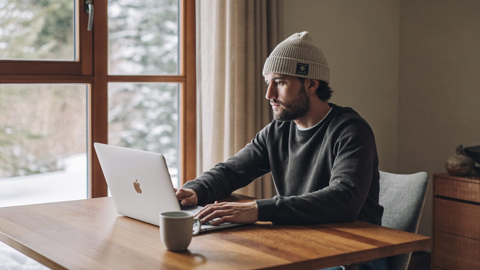 Man in his 30s with thick, healthy hair working on a laptop at a home desk by a window with autumn light